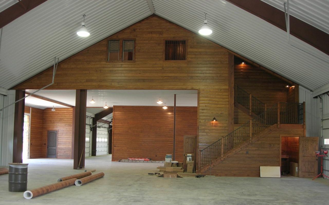 Barndominium interior with wood-paneled walls and stairs to the living quarters, built by Cross Creek