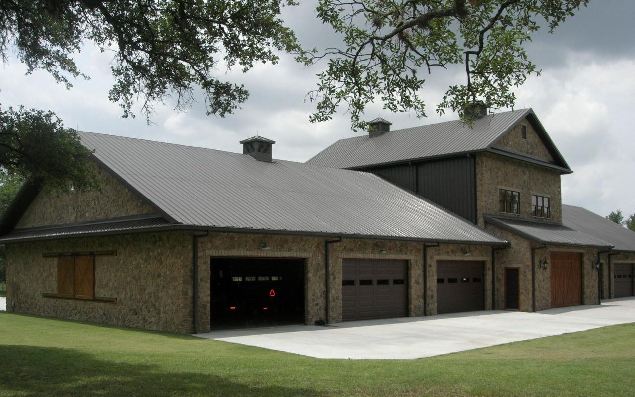 Front of a stone barndominium under live oaks, built by Cross Creek