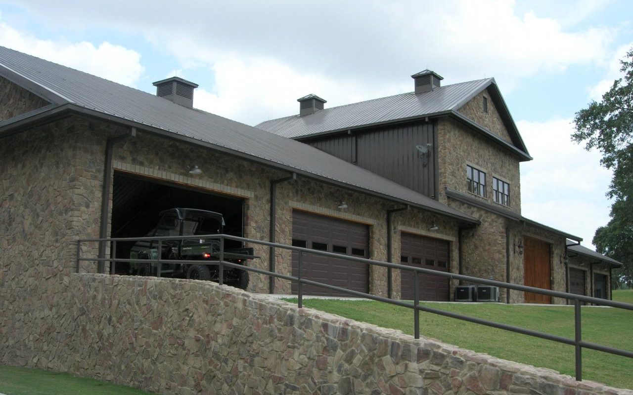 Stone barndominium with rock retaining wall and upstairs balcony, built by Cross Creek