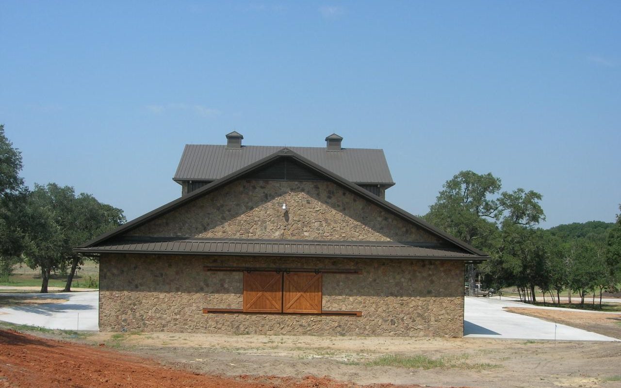 Side view of a stone barndominium with a metal roof and cupola, built by Cross Creek