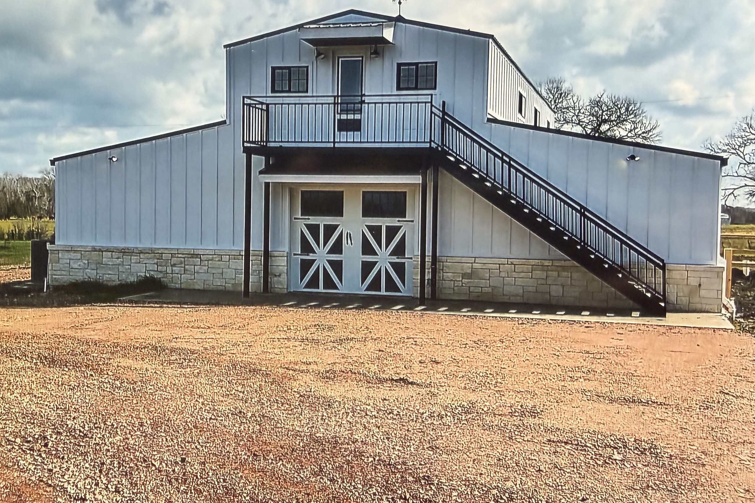 White barndominium with a stone base, upstairs deck, and exterior stairs, built by Cross Creek