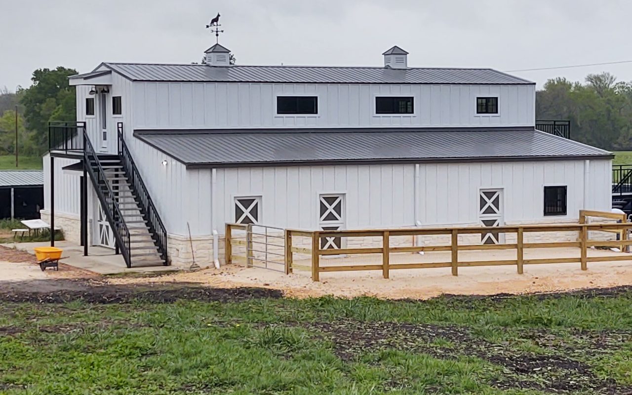 White board and batten barndominium with a stone base, cupolas, and an upstairs deck, built by Cross Creek