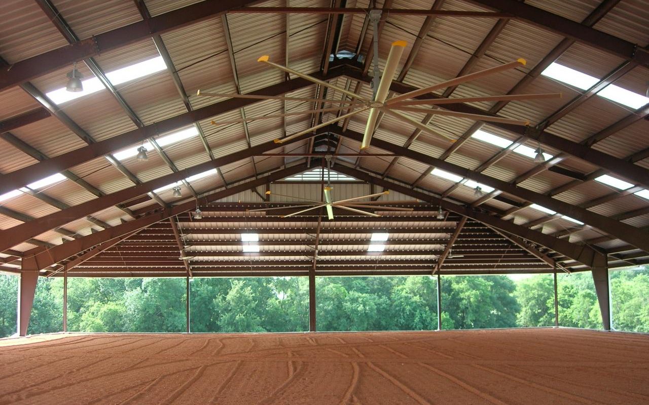 Inside a covered riding arena with steel trusses and groomed footing