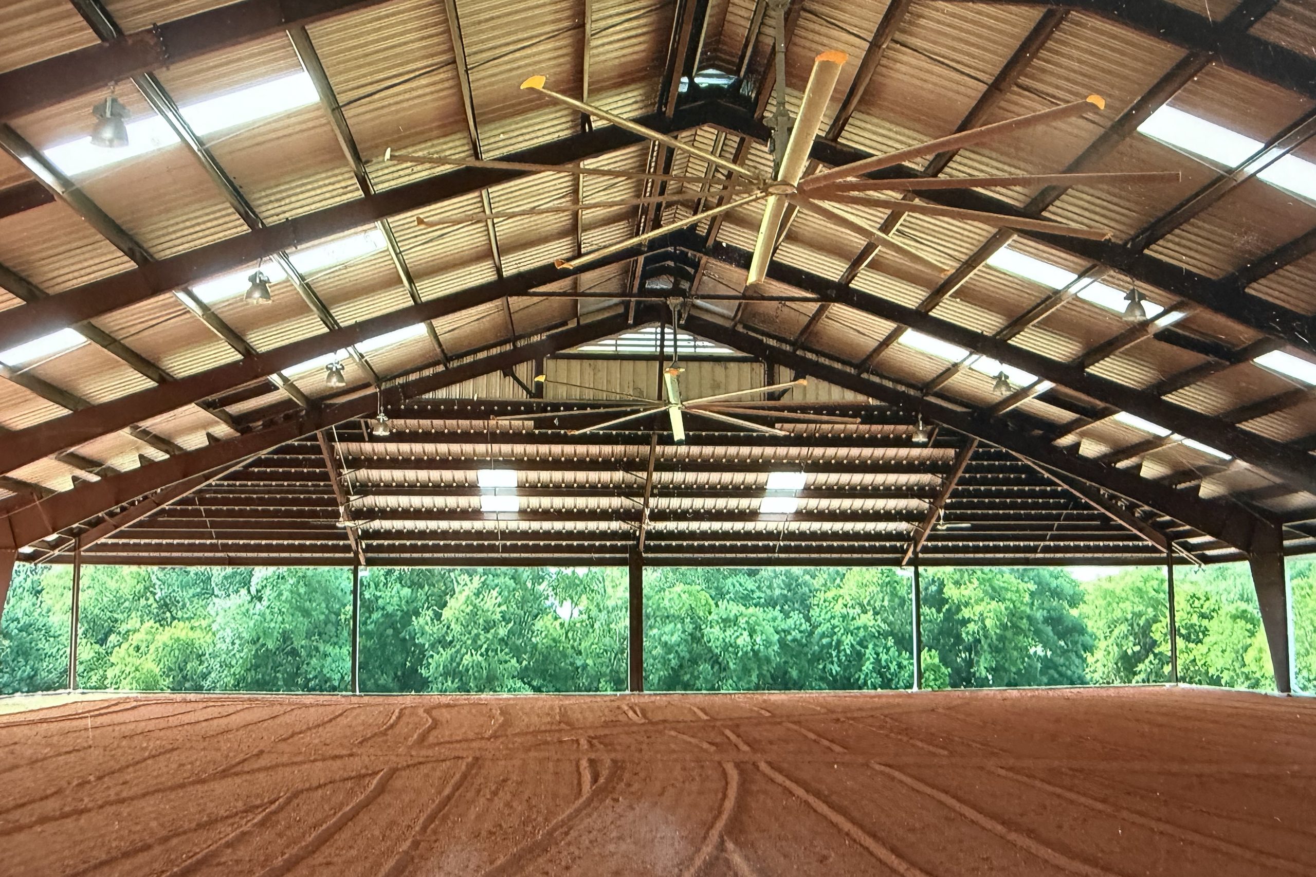 Inside a covered riding arena with steel trusses and open sides, built by Cross Creek