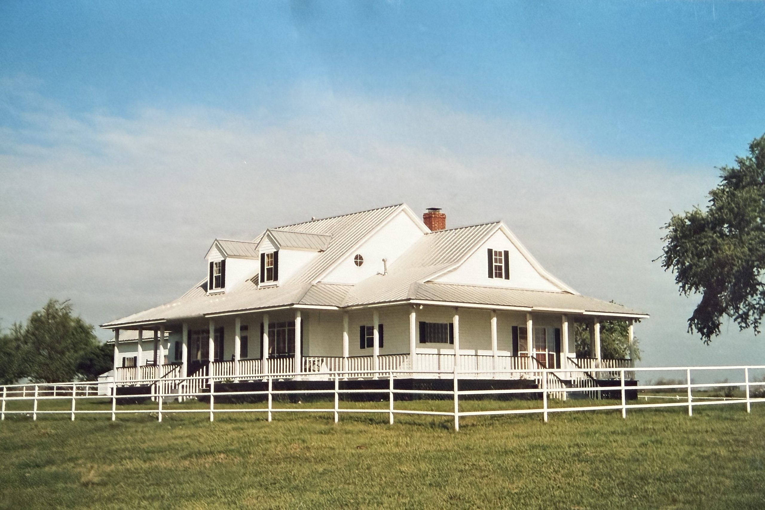 White custom farmhouse with dormers and a wraparound porch, built by Cross Creek
