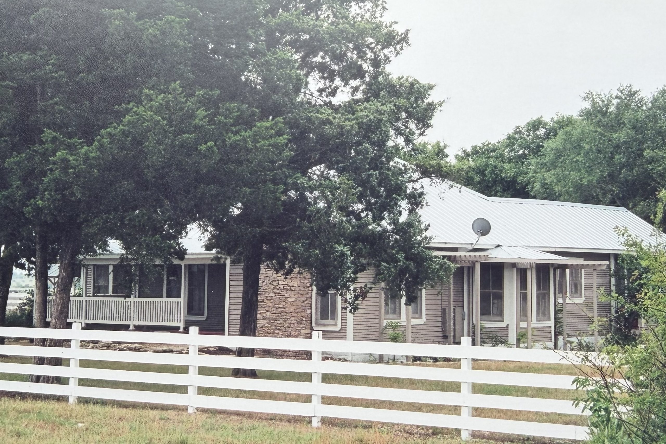 Custom ranch home with a wraparound porch behind a white board fence, built by Cross Creek