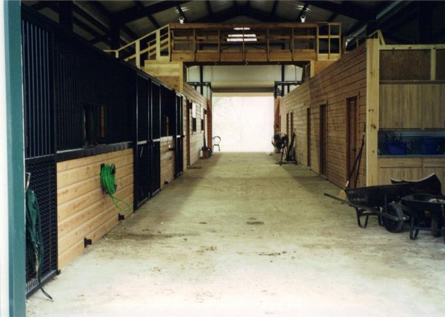 Center aisle with custom stalls inside a Cross Creek horse barn